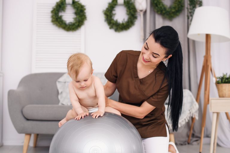 a-professional-female-masseuse-with-happy-baby-doing-exercises-with-fitness-ball-at-medical-room-healthcare-and-medical-concept